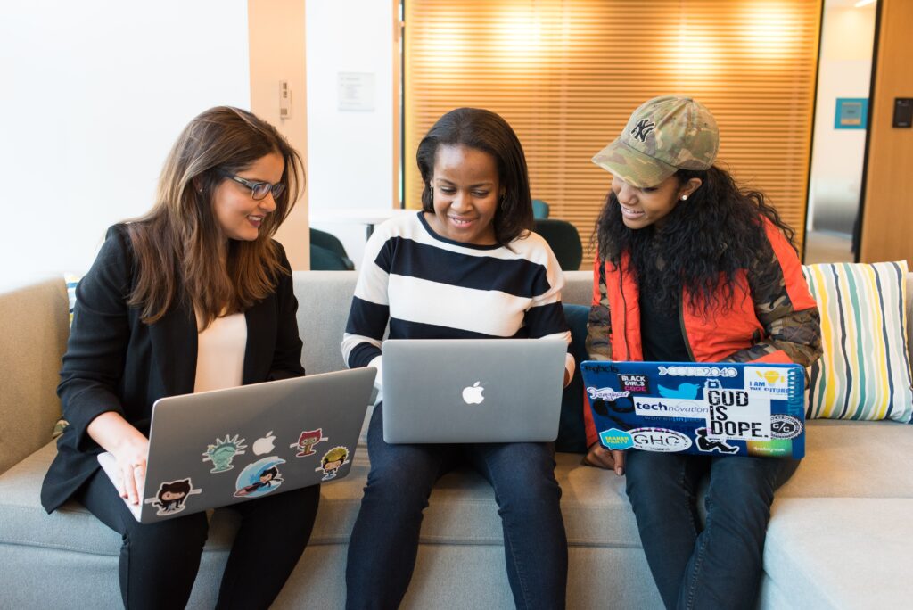 Image description: three women sitting on a couch with laptops working together
